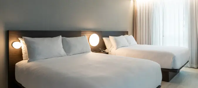 Modern hotel room with two queen beds, bedside lighting, and floor-to-ceiling curtains at Burlington Square