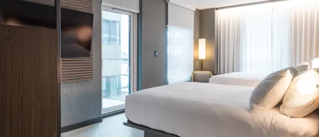 Modern guest room with two beds, floor-to-ceiling windows, and contemporary furnishings at Burlington Square
