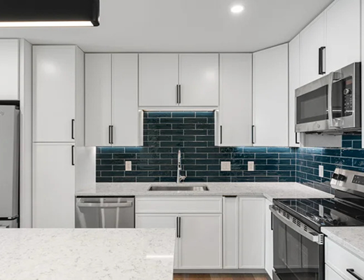 Modern apartment kitchen with white cabinetry, stainless steel appliances, quartz countertops, and blue tile backsplash at Burlington Square Apartments