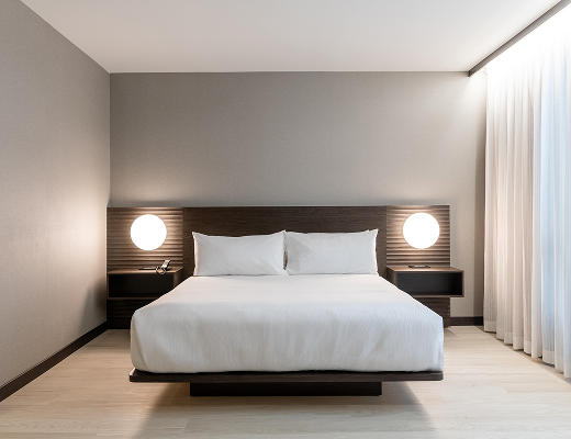Modern king guest room at AC Hotel Burlington featuring a platform bed, bedside lighting, and floor-to-ceiling curtains